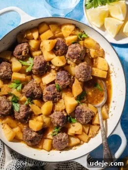 A white pan filled with meatballs, potatoes, and sauce, garnished with parsley.