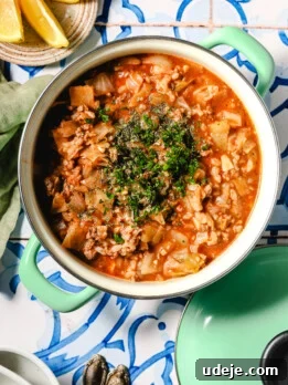 A pot of hearty stew with ground meat, chopped vegetables, and tomato sauce, garnished with fresh herbs.