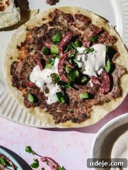 Kofta smash taco topped with cucumber and onions with white sauce on a beige plate.