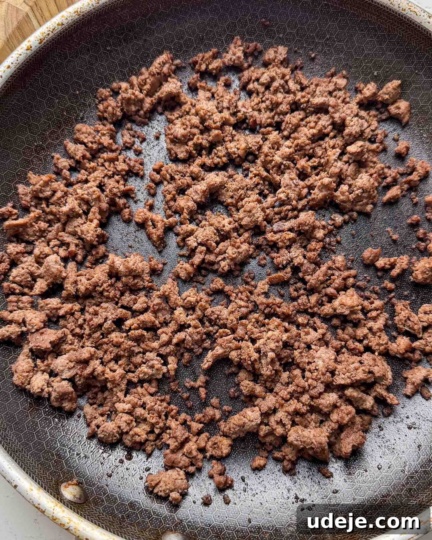 Cooked ground beef scattered in a nonstick frying pan, with a honeycomb-textured surface visible underneath the browned meat.