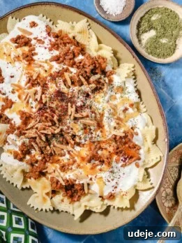 A platter of bowtie pasta topped with seasoned ground meat, creamy white sauce, slivered almonds, herbs, and spices.