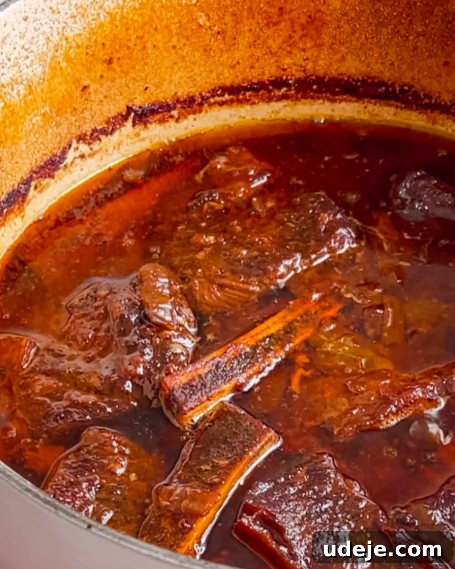 Fall-Apart Pomegranate Beef Short Ribs (No Wine) 6 Chunks of beef short ribs simmer in a rich, dark brown sauce inside a large pot with browned edges, indicating slow cooking and tender meat.