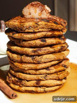 Stack of fluffy pumpkin chocolate chip pancakes topped with maple cinnamon butter and drizzled with maple syrup